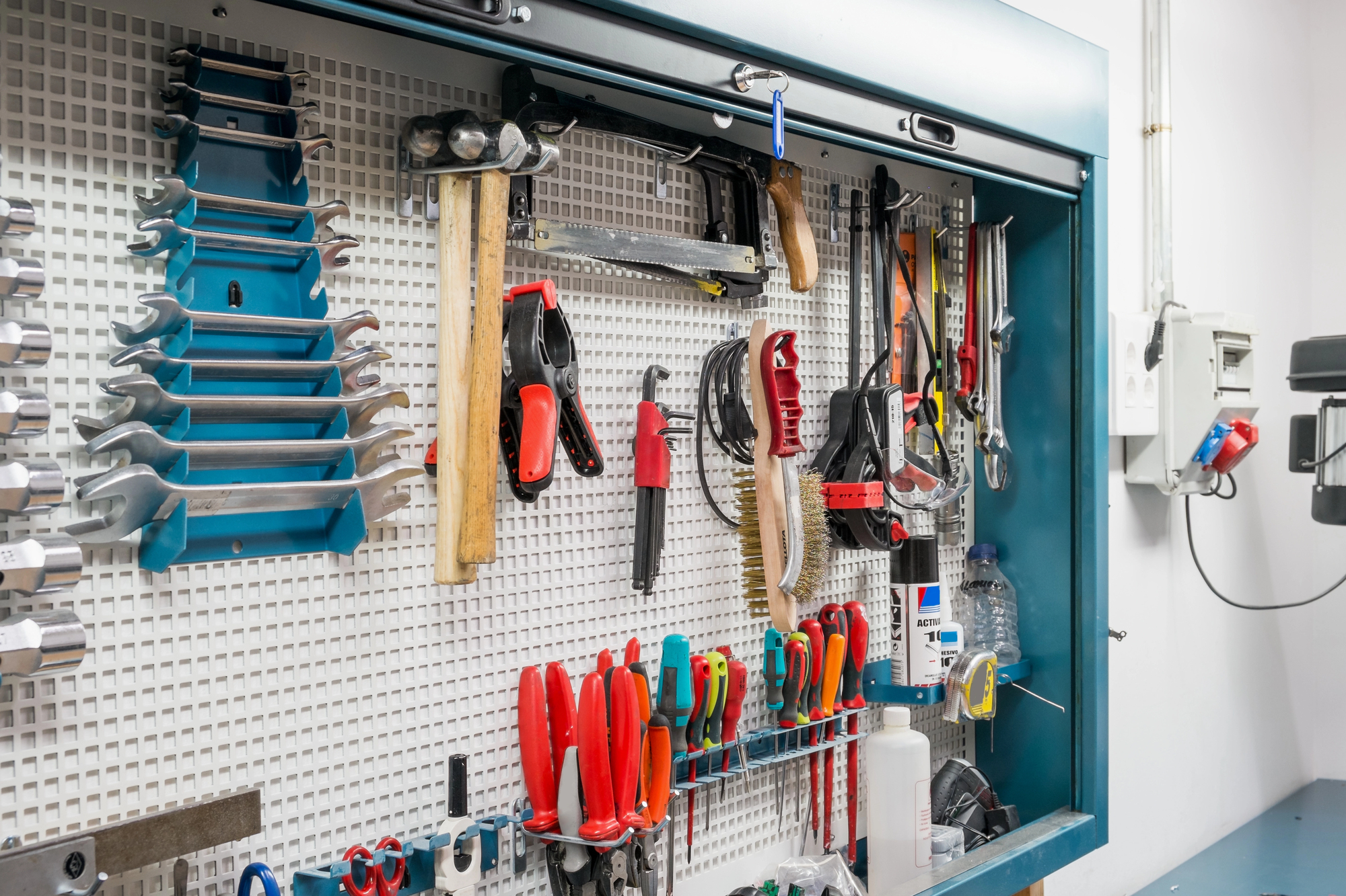 A neatly organized tool cabinet with various hand tools including hammers, screwdrivers, pliers, wrenches, and brushes mounted on a white pegboard.